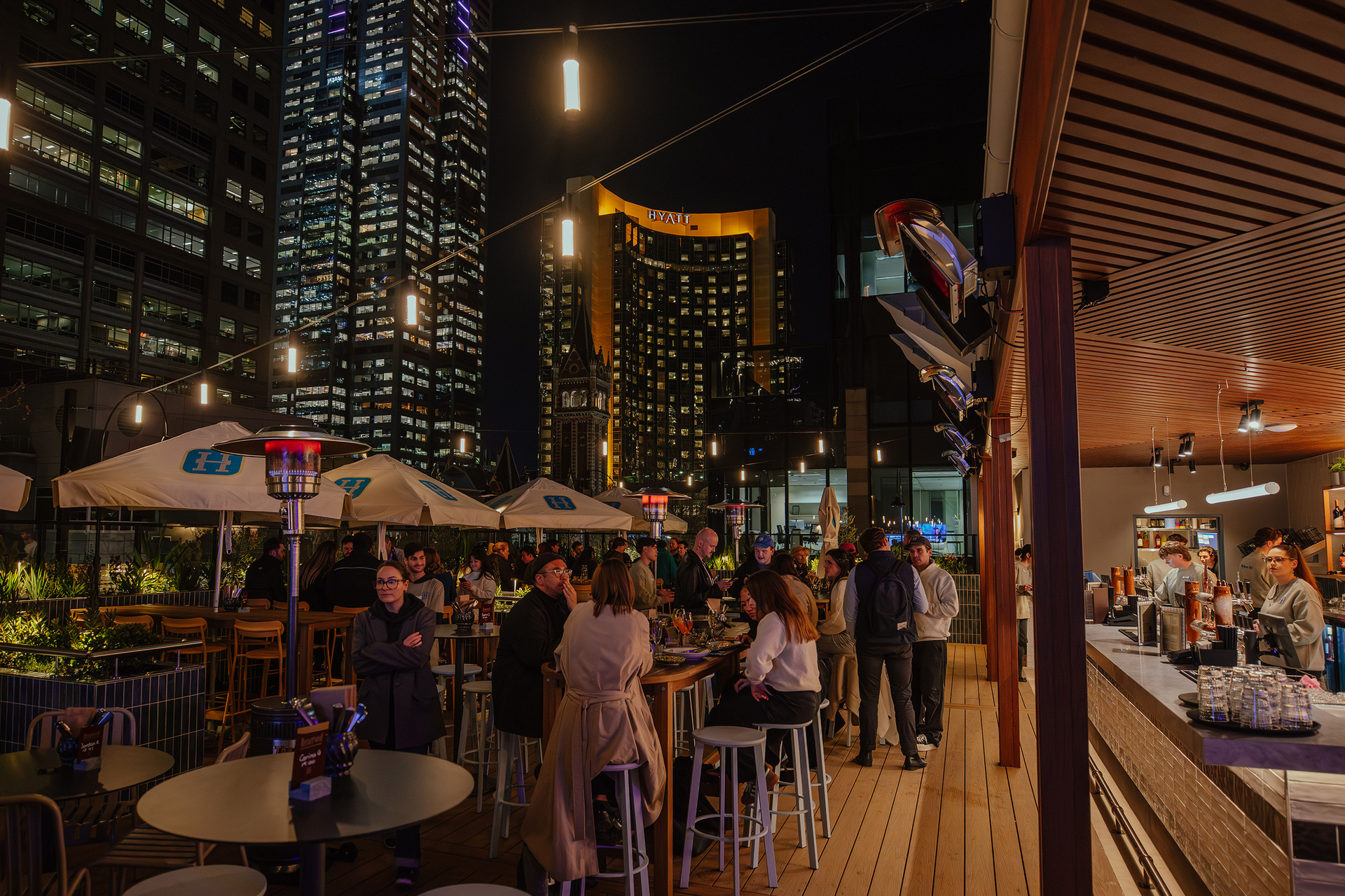 A busy rooftop pub at night with a view of the city skyline