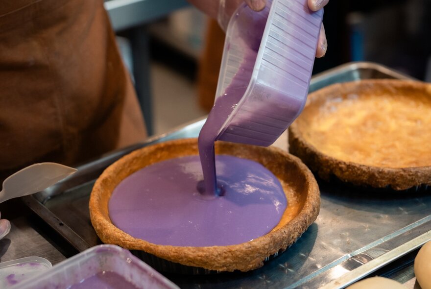 Purple sauce being poured into a pastry case.