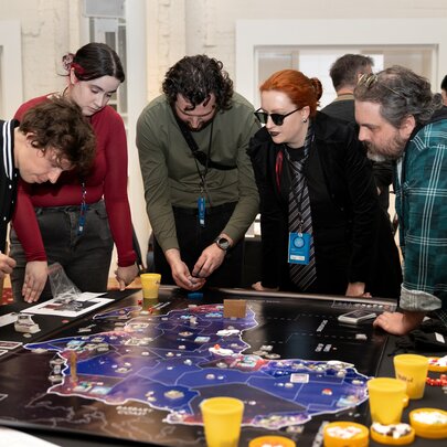 A group of people standing over a game table playing a strategy board game.