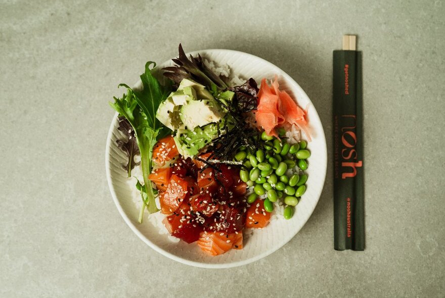 Japanese-inspired poke bowl with delicious wholefood ingredients alongside chopsticks, on a grey surface.