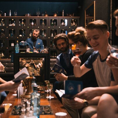 A group of people seated around a low table taking part in an interactive cocktail masterclass, a bartender in the background.