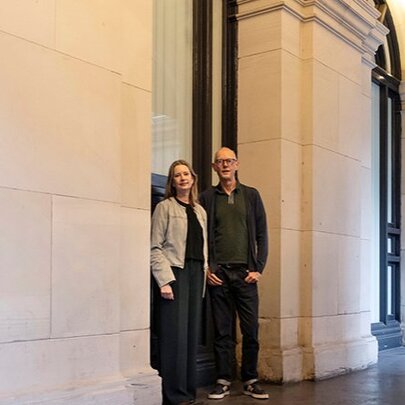 Two people standing in a grand portico with stone arches.
