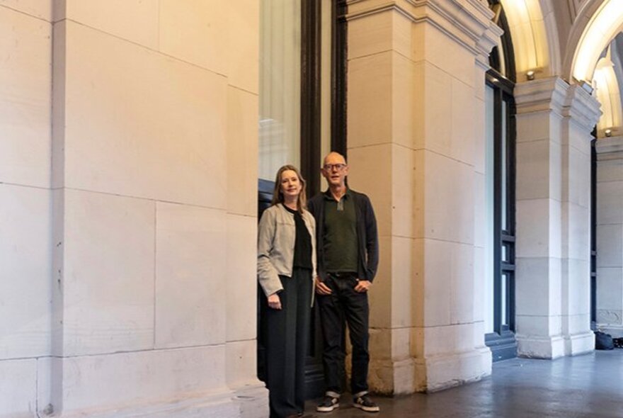 Two people standing in a grand portico with stone arches.