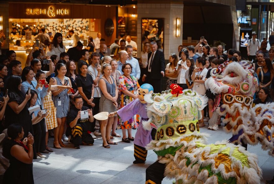 People watching a dragon dance performance in an indoor shopping mall.