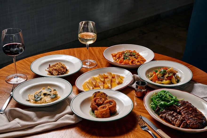 A round, wooden table laden with plates of delicious food and glasses of wine.
