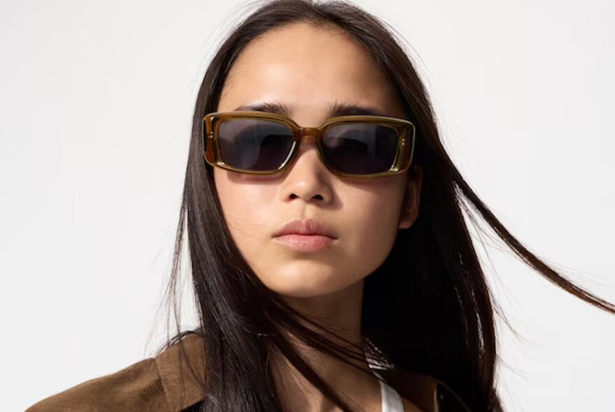 A young woman with straight black hair wearing brown, square-framed UNIQLO sunglasses.