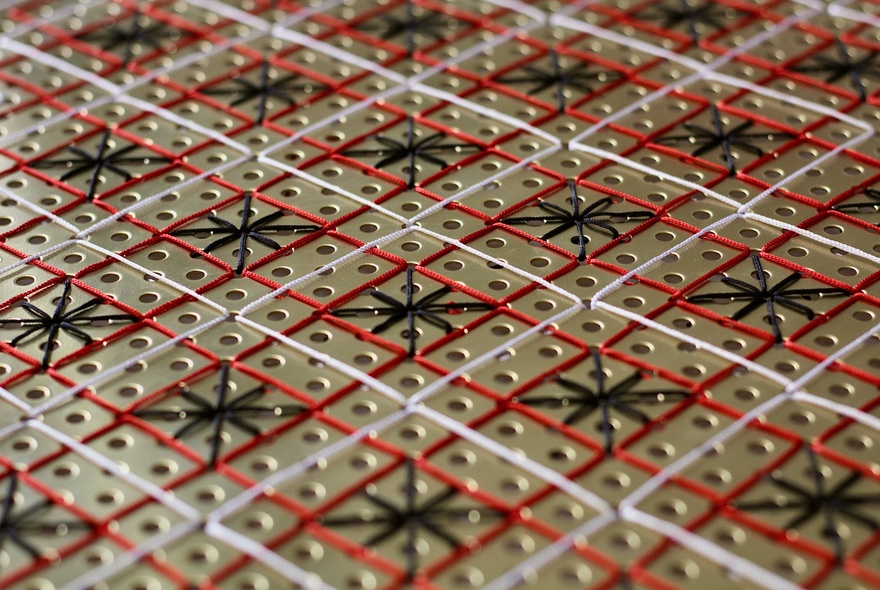 A close-up of a metallic artwork featuring grids in orange and white with black star patterns. 