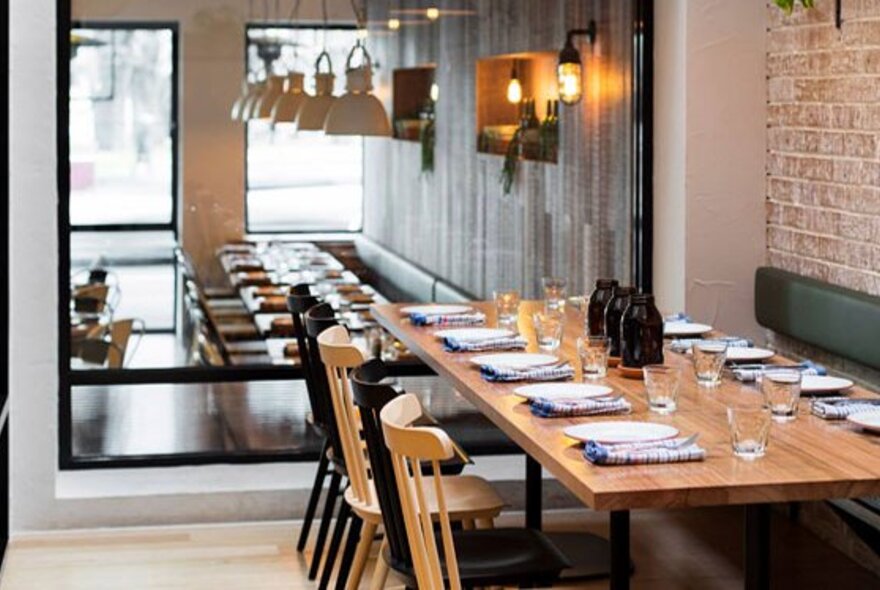 An empty long table in a restaurant, set for service. 