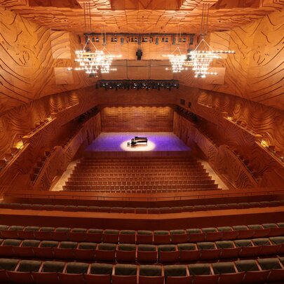 The warm-toned interior of the Melbourne Recital Centre with a central stage with a purple light and piano. 