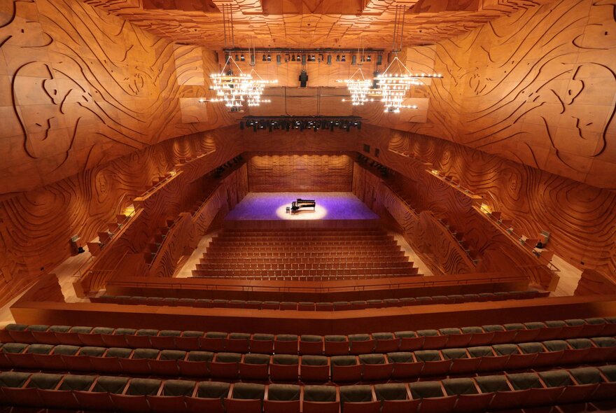 The warm-toned interior of the Melbourne Recital Centre with a central stage with a purple light and piano. 