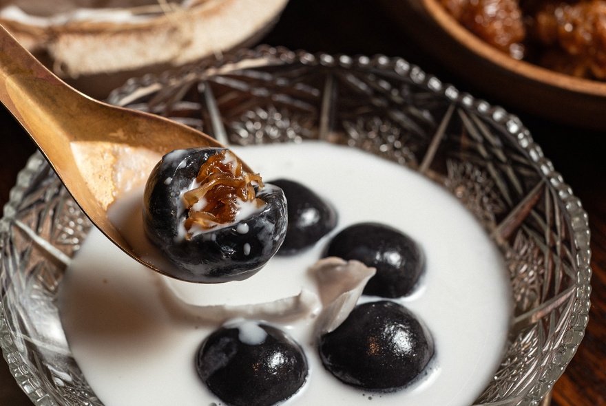 A Thai delicacy of black balls in white sauce, one shown on a bronze spoon opened up to show a spiky brown core.