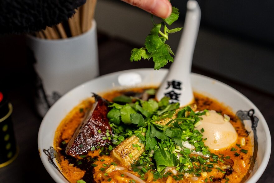 A deep bowl filled with ramen broth, garnished with chopped parsley.
