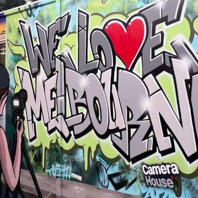 A person taking a photograph of a graffiti wall that says 'I Love Melbourne'