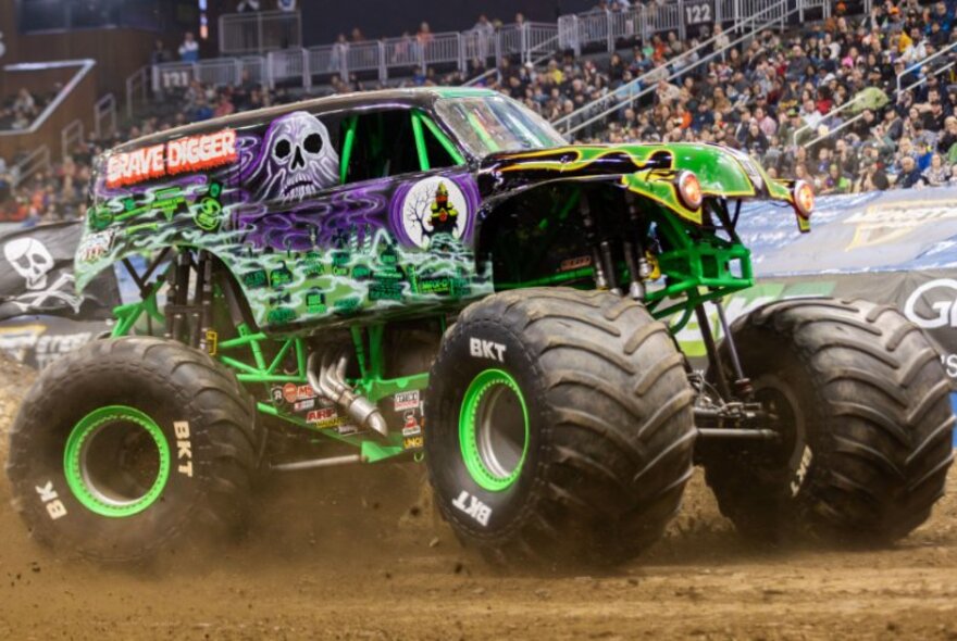 A monster truck called Grave Dinner in an arena with a crowd looking on, kicking up dust. 