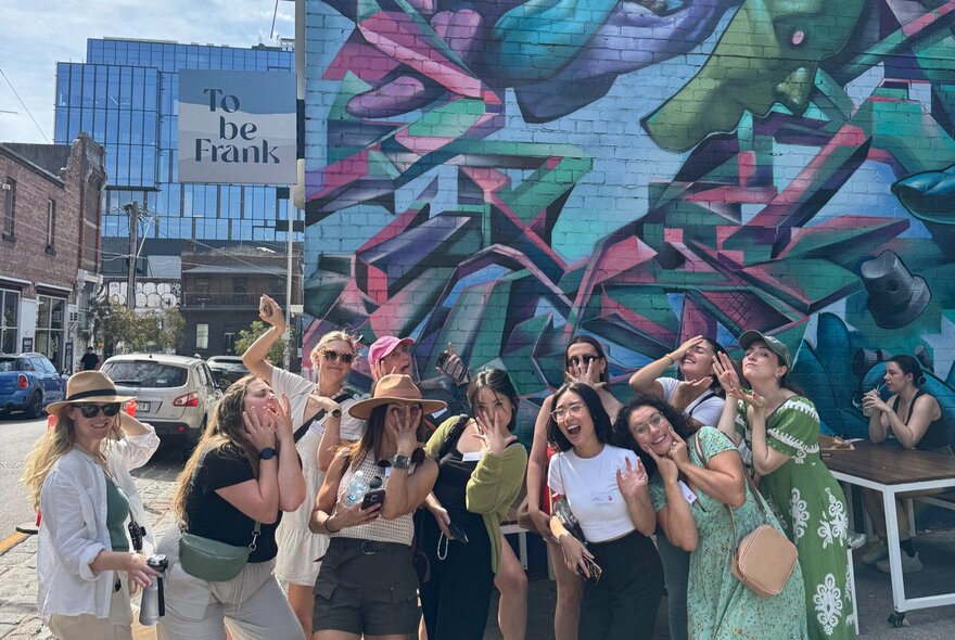 A group of women in the city looking excited in front of a painted wall.