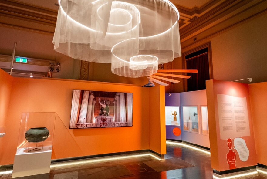 A gallery space with orange walls and an elaborate light with spiral features. 