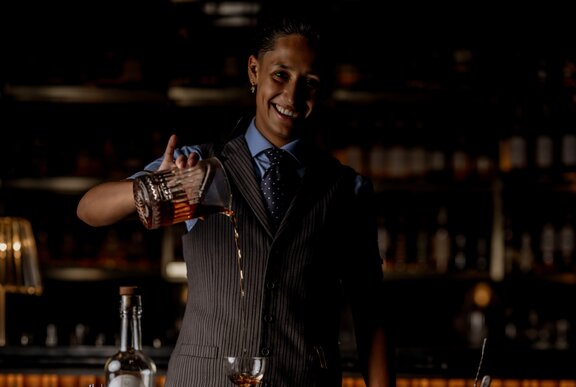 Head bartender from Manhattan Singapore, Zana, pouring a cocktail from a glass beaker into a glass.