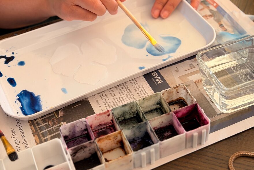Hands using a brush to mix blue dye in a plastic tray.