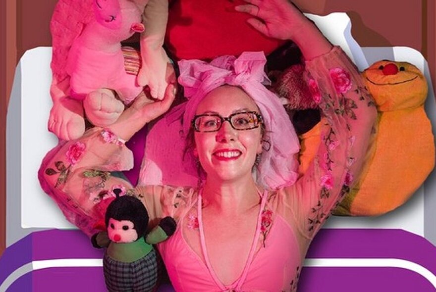 Looking down at a smiling performer lying on a bed, surrounded by soft toys and pillows.