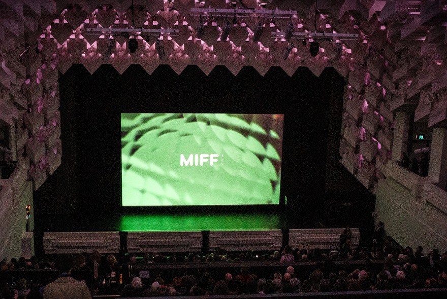 The interior of The Capitol theatre during a Melbourne International Film Festival screening, with a seated audience and a large screen displaying the MIFF logo on a green background.