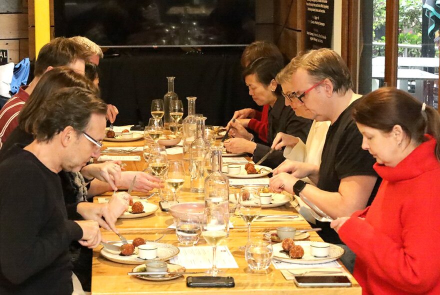 Dining patrons seated around a long table in a restaurant, eating and drinking. 