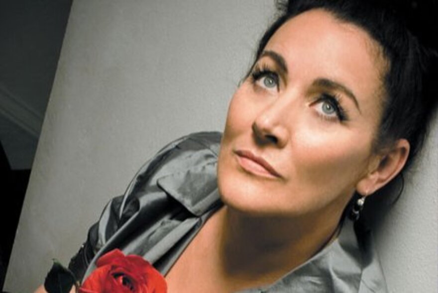 Grace Knight, woman with dark hair, piled on top of head, leaning against a wall and looking upwards.