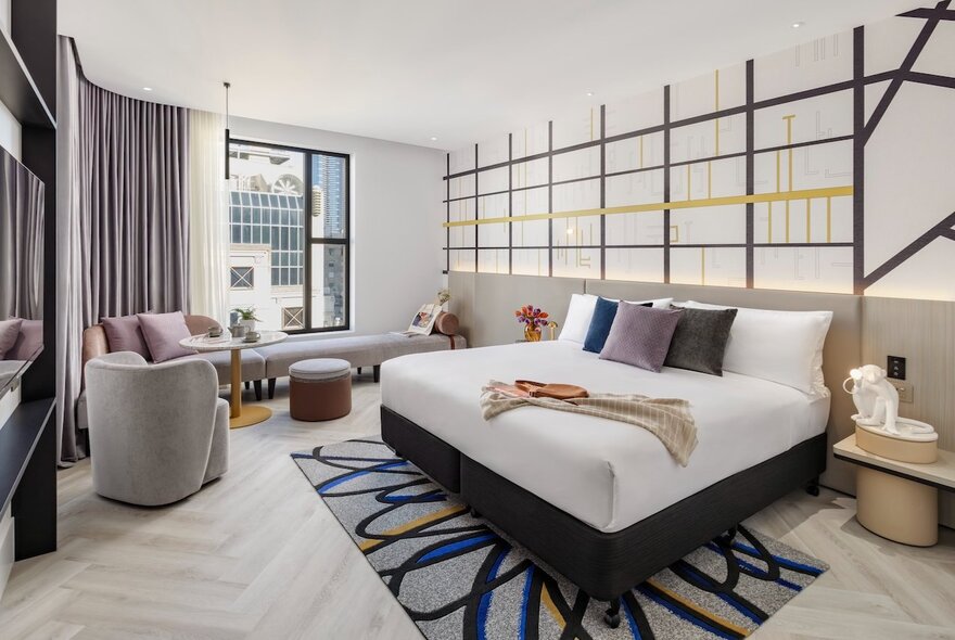 A room at Hotel Indigo, with Mondrian inspired stripes on the wall, a king bed, soft furnishings and a large window.