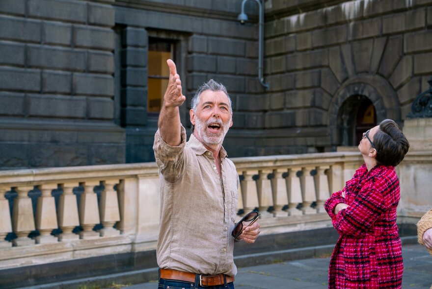 A tour leader pointing at something in the distance while a woman in a red coat stares up in the other direction. 