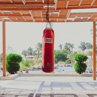 A red sports boxing punching bag hanging from the verandah ceiling in an outdoor setting.