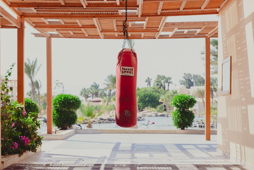A red sports boxing punching bag hanging from the verandah ceiling in an outdoor setting.