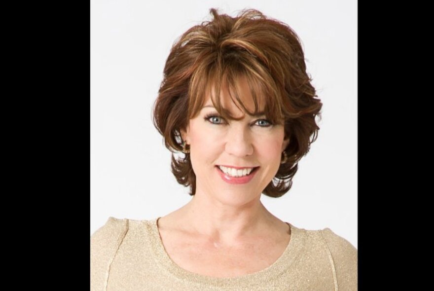 Portrait of author, Kathy Lette, smiling directly at the camera.