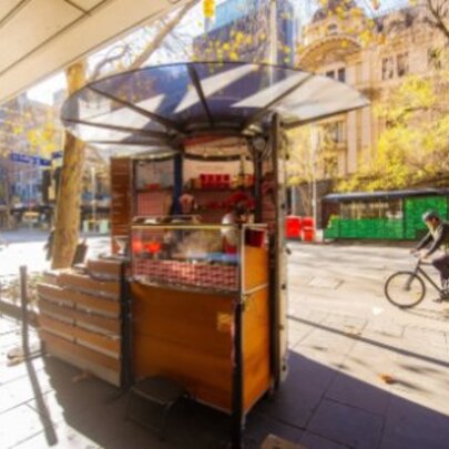 Creperie cart in winter sunshine with dappled light through trees as a cyclist passes on an empty street.