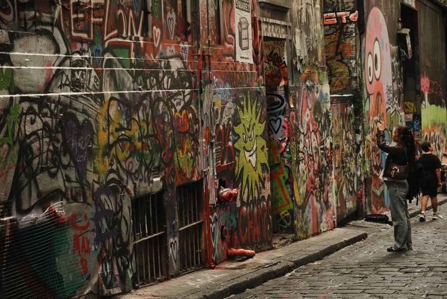 Person taking a photo in a graffitied laneway.