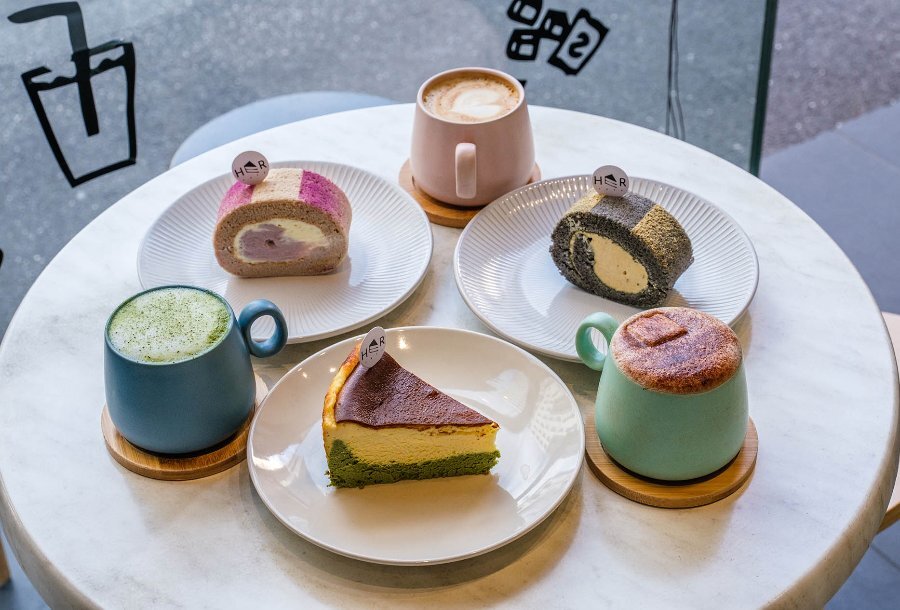 An assortment of colourful cakes and lattes on a white marble table.