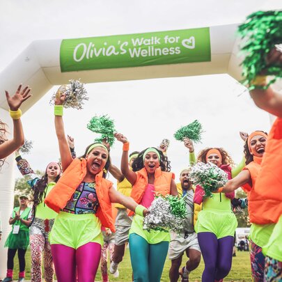 Walkers entering the finish line of a charity walk, wearing brightly coloured running shorts and leggings.