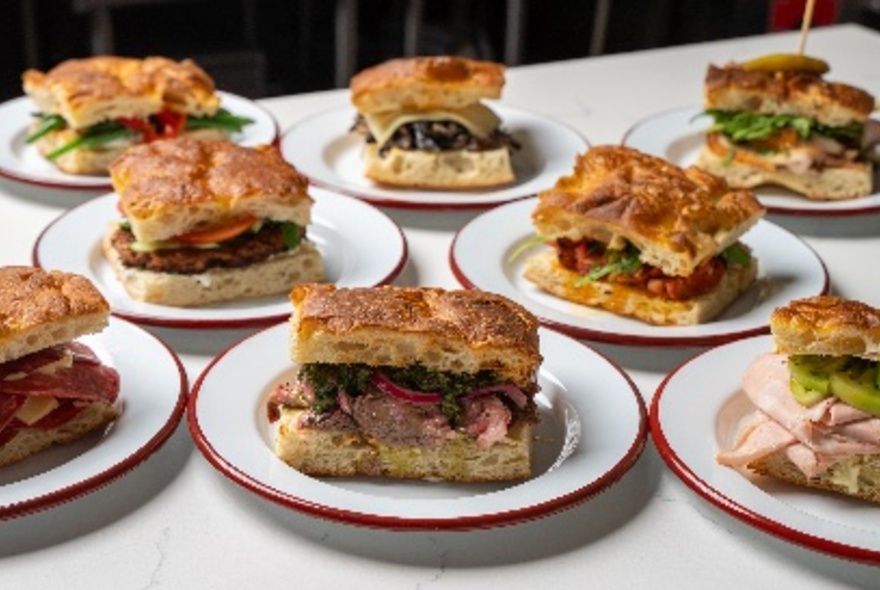 Filled focaccias on eight white plates on a table.