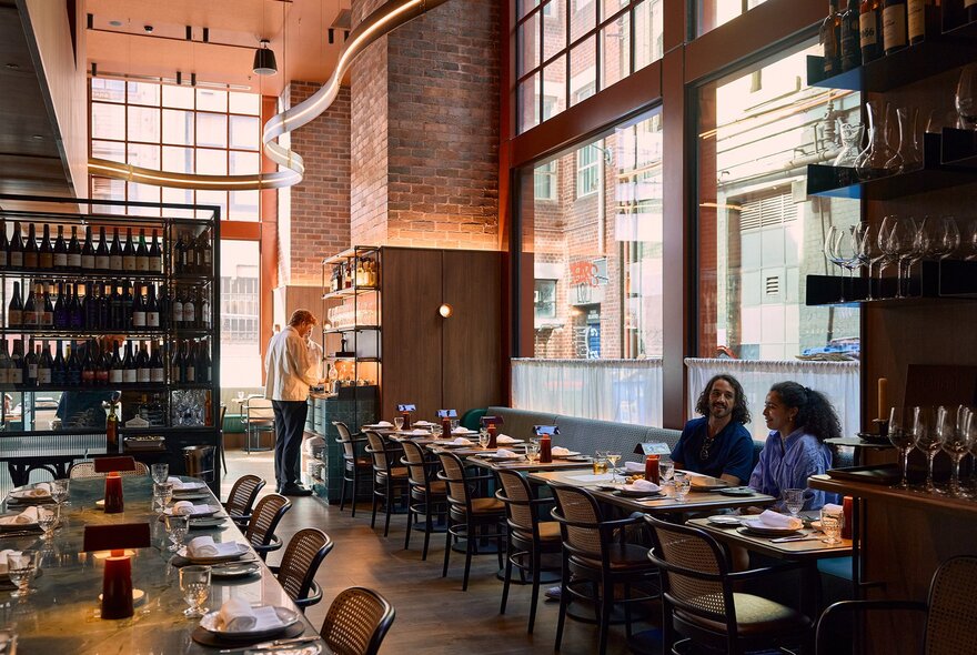 A couple sharing a meal in a restaurant with high ceilings, candles and wine bottles.
