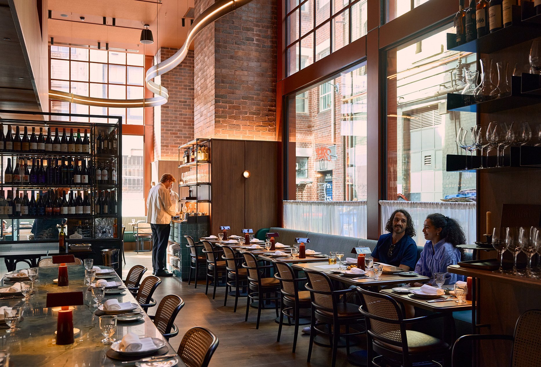 A couple sharing a meal in a restaurant with high ceilings, candles and wine bottles.