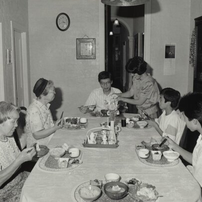 A black and white photograph of a family eating a meal at the family dining table circa 1950.
