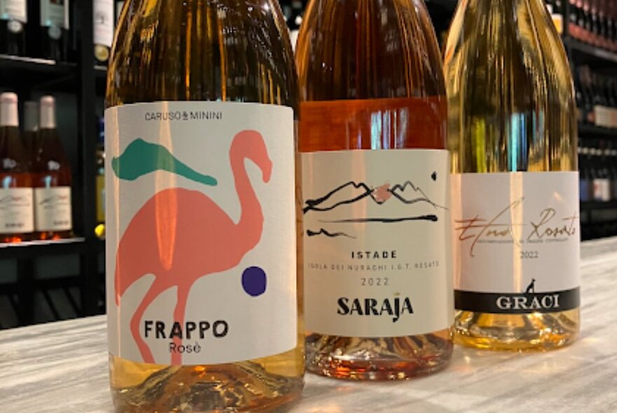 Bottles of rosé wine on a counter with other bottles on shelves in the background.