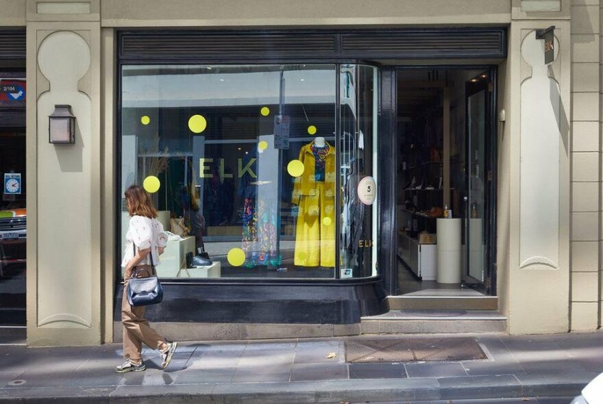 A woman walking past a shop with yellow clothing in the window. 