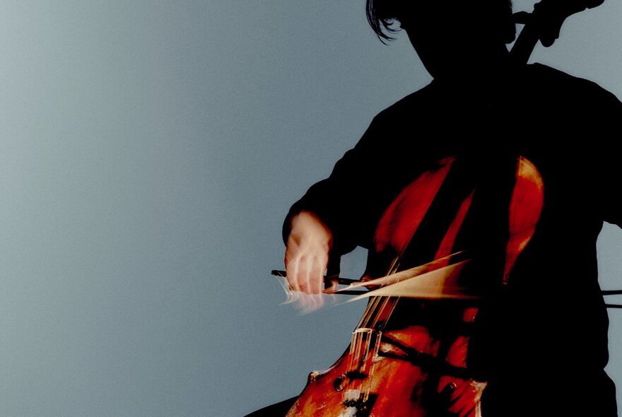 A person, with their face in the shadows, playing a cello