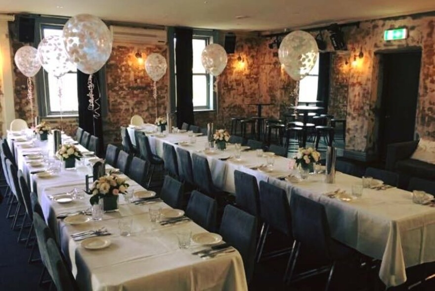 Two long restaurant tables with white table cloths and set for meals.