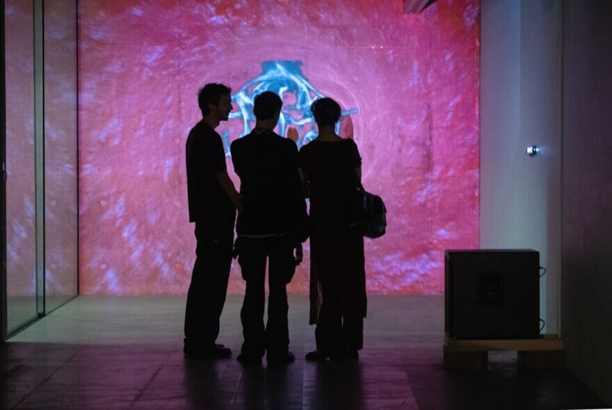 People looking at a large-scale pink wall mural artwork in a gallery space.