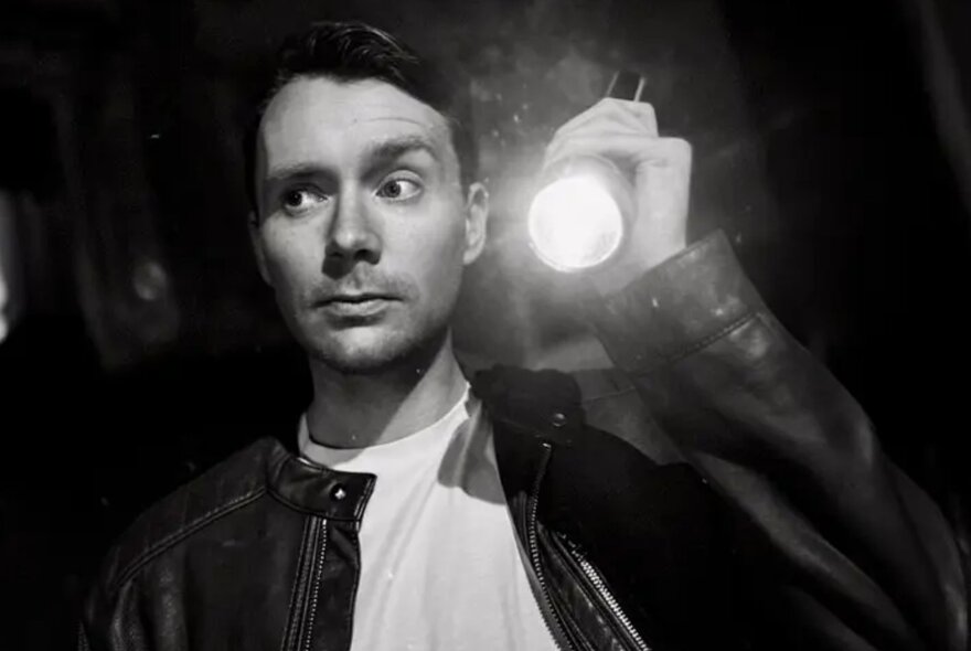 A black and white portrait of a man wearing a leather jacket and holding up a torch.