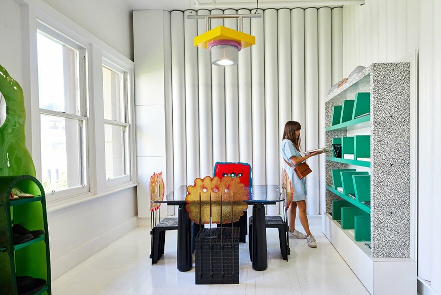 A woman browsing a green bookshelf in an aesthetic furniture display in a store.