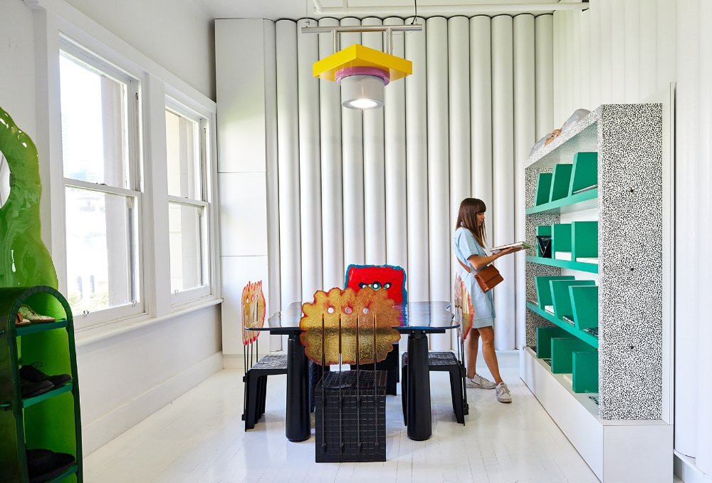 A woman browsing a green bookshelf in an aesthetic furniture display in a store.