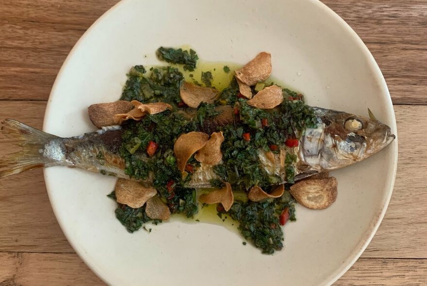 A fish covered with green sauce on a plate on a wooden table.