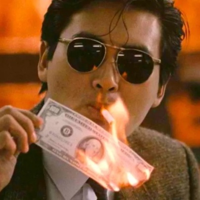 A still from the movie A Better Tomorrow, with a man wearing dark glasses lighting a cigarette with a burning banknote.