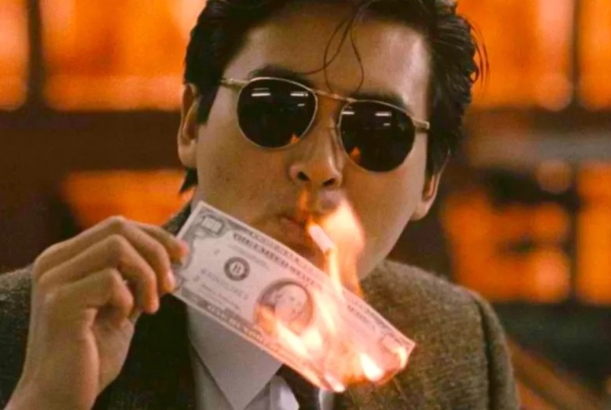 A still from the movie A Better Tomorrow, with a man wearing dark glasses lighting a cigarette with a burning banknote.
